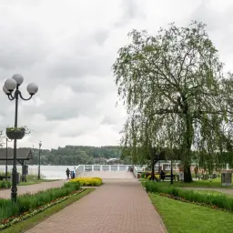 Spacer w Mrągowie nad jeziorem, z wierzbą płaczącą i kwitnącymi rabatami. Atrakcje dla spacerowiczów.