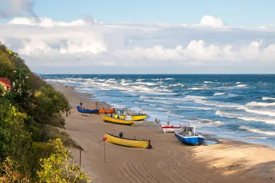 Kolorowe łodzie rybackie na piaszczystej plaży, falujące morze i zielone wzgórze tworzą malowniczy widok polskiego morza.