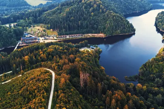 Malownicze jezioro w Zagórzu Śląskim otoczone jesiennymi lasami. W oddali widać zabudowania ośrodka wypoczynkowego.