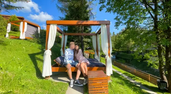 Para zakochanych siedzi na łóżku pod baldachimem, idealny pomysł na weekend w otoczeniu zieleni i strumienia.