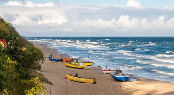 Kolorowe łodzie rybackie na piaszczystej plaży, falujące morze i zielone wzgórze tworzą malowniczy widok polskiego morza.